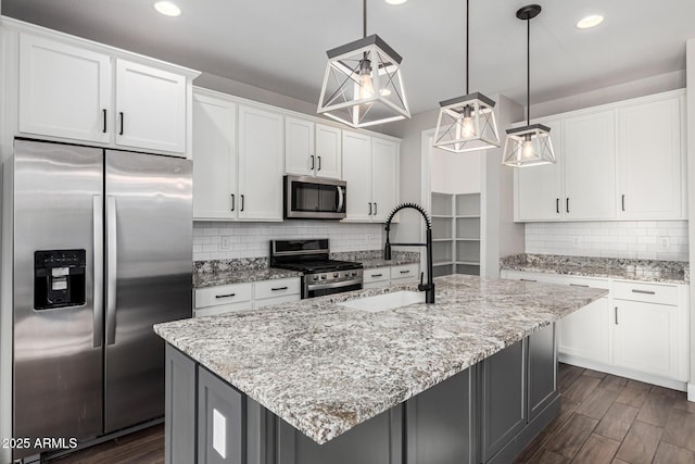 kitchen featuring appliances with stainless steel finishes, an island with sink, white cabinetry, sink, and hanging light fixtures