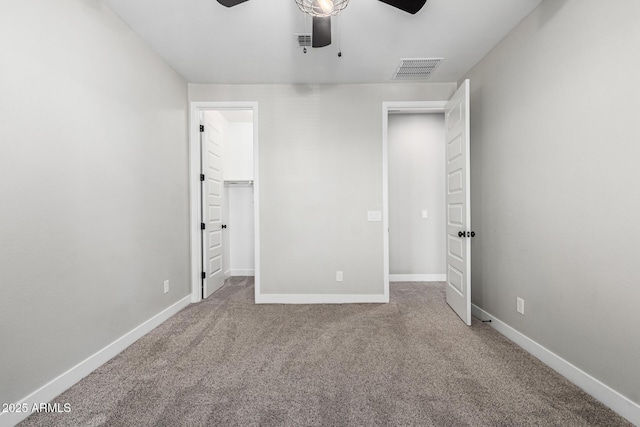 unfurnished bedroom with a walk in closet, ceiling fan, and carpet flooring