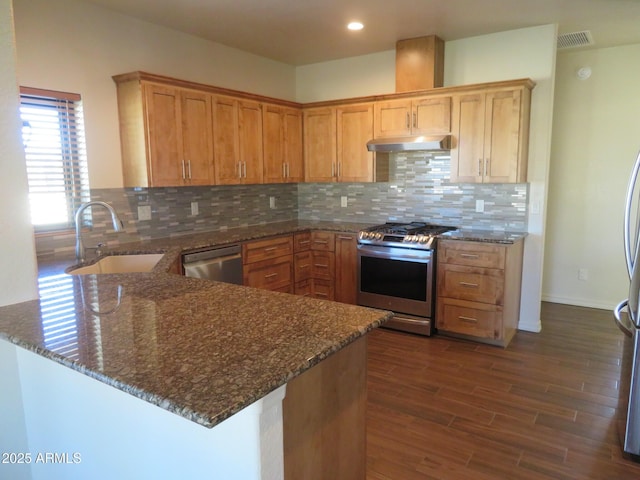 kitchen featuring sink, stainless steel appliances, tasteful backsplash, kitchen peninsula, and dark stone counters