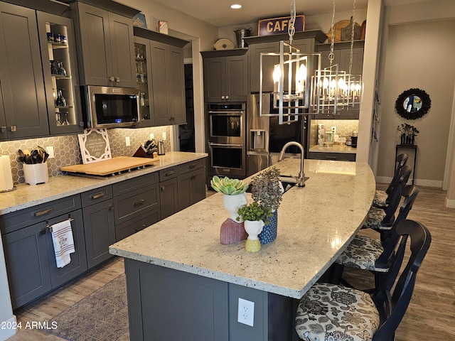 kitchen featuring appliances with stainless steel finishes, hardwood / wood-style flooring, hanging light fixtures, and an island with sink