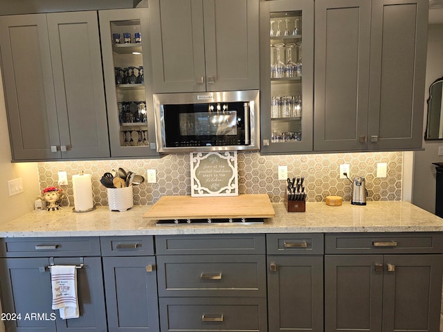 bar with decorative backsplash, gray cabinets, and light stone counters