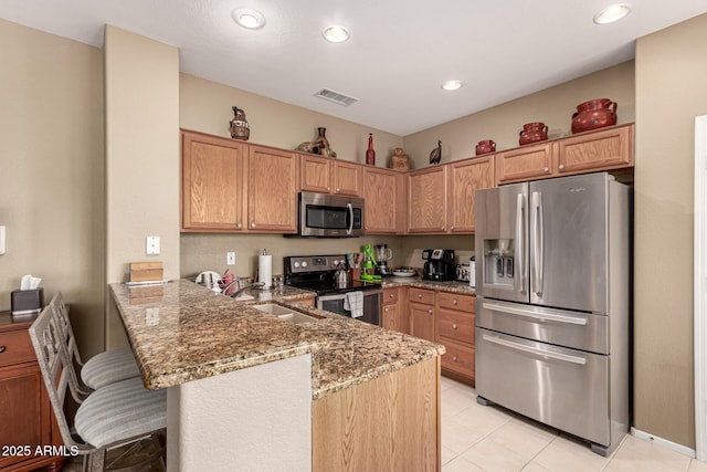 kitchen featuring stainless steel appliances, a peninsula, a sink, visible vents, and light stone countertops