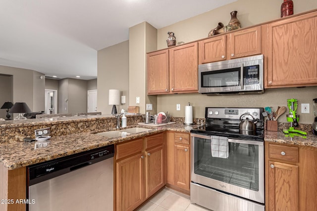 kitchen with light tile patterned floors, appliances with stainless steel finishes, a sink, and light stone countertops