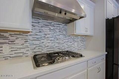 kitchen with white cabinetry, black fridge, extractor fan, and backsplash