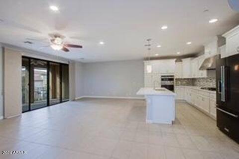 kitchen with tasteful backsplash, black fridge, white cabinets, and a center island with sink