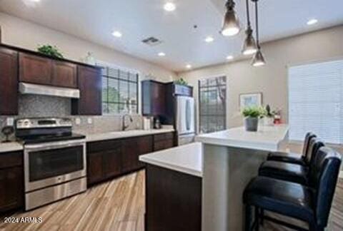 kitchen featuring decorative light fixtures, a breakfast bar area, backsplash, electric range, and dark brown cabinetry