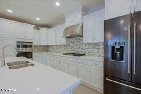 kitchen featuring stainless steel refrigerator with ice dispenser, ventilation hood, sink, and white cabinets