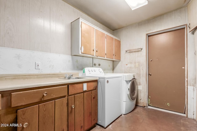 laundry area with cabinets, washer and clothes dryer, wood walls, and sink