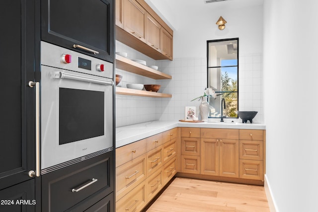 kitchen featuring open shelves, a sink, backsplash, light wood finished floors, and white oven