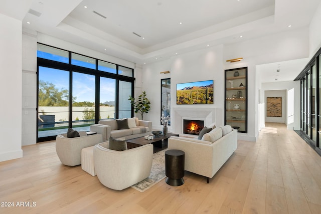 living room featuring light wood finished floors, a raised ceiling, a towering ceiling, and a high end fireplace