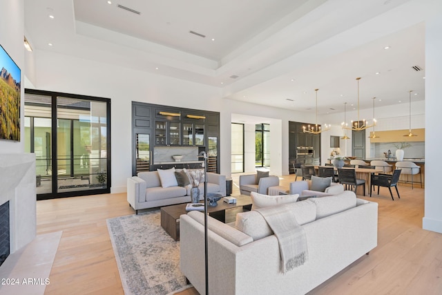 living room featuring a notable chandelier, light wood-style flooring, a high ceiling, a premium fireplace, and a raised ceiling