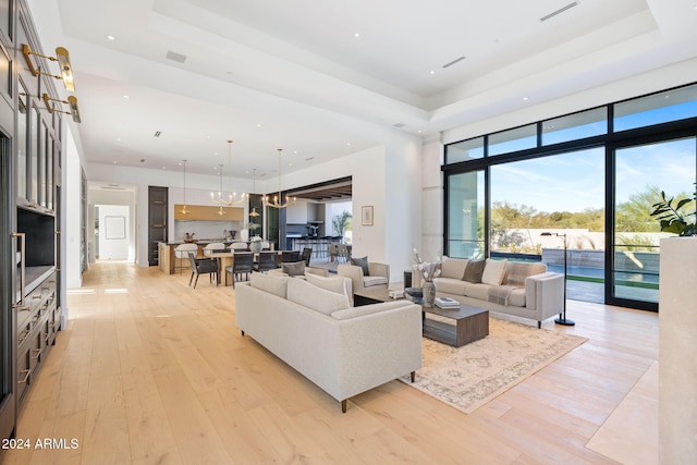 living room featuring a chandelier, visible vents, light wood-style flooring, and a raised ceiling