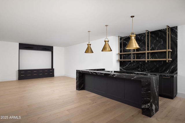 interior space featuring dark stone counters, light wood-style floors, pendant lighting, and dark cabinets