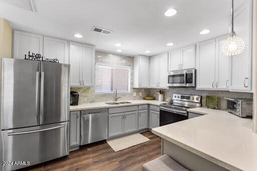 kitchen with stainless steel appliances, sink, backsplash, hanging light fixtures, and dark hardwood / wood-style floors