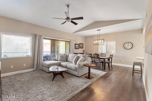 living room featuring ceiling fan with notable chandelier, dark hardwood / wood-style floors, and vaulted ceiling