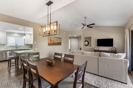 dining space with ceiling fan with notable chandelier, sink, wood-type flooring, and lofted ceiling