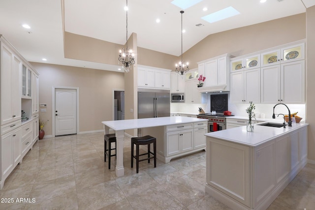 kitchen featuring a skylight, a kitchen island with sink, sink, built in appliances, and white cabinets