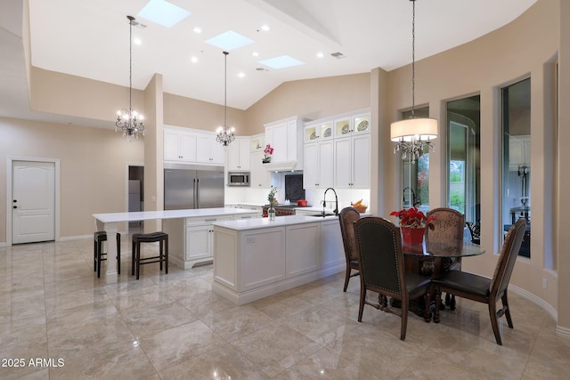 kitchen with built in appliances, white cabinets, an island with sink, and a skylight