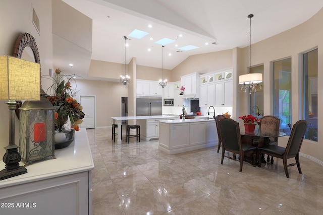 kitchen featuring a center island with sink, sink, a skylight, decorative light fixtures, and white cabinetry