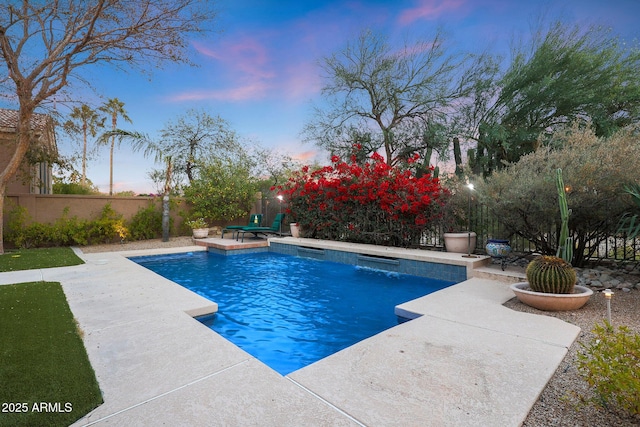 pool at dusk with pool water feature and a patio area