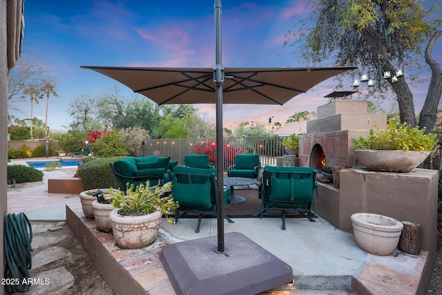 patio terrace at dusk with an outdoor living space with a fireplace and a fenced in pool