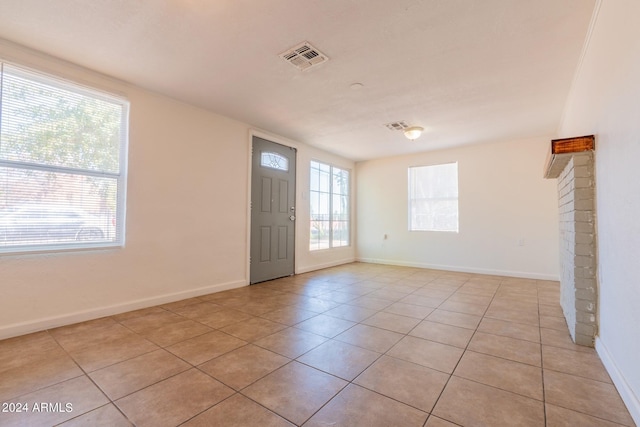 foyer entrance featuring light tile patterned floors, a brick fireplace, and plenty of natural light