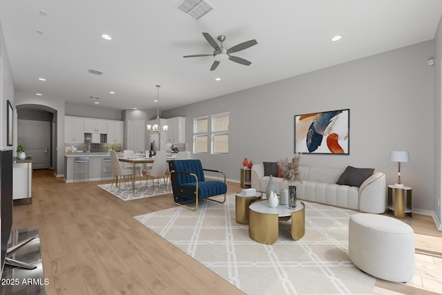 living room with light hardwood / wood-style floors and ceiling fan with notable chandelier