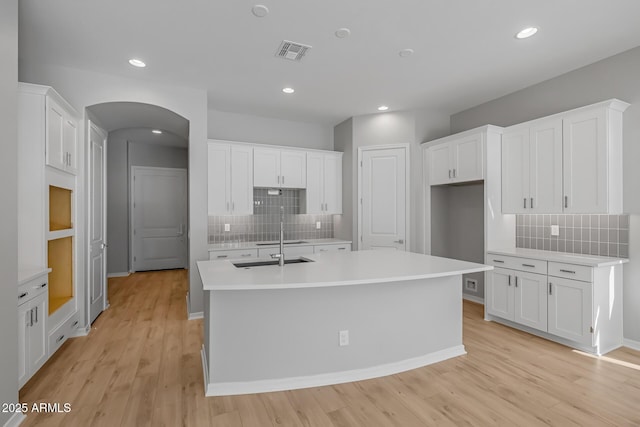 kitchen featuring a center island with sink, white cabinetry, and tasteful backsplash