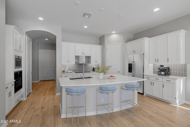 kitchen featuring a kitchen breakfast bar, a center island with sink, white cabinets, and appliances with stainless steel finishes