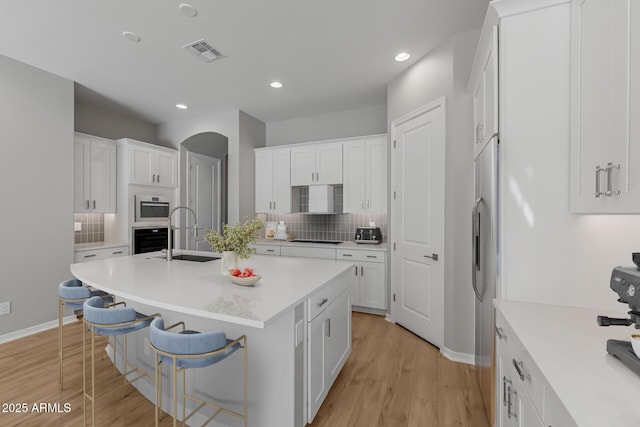 kitchen featuring white cabinets, a center island with sink, sink, black oven, and a breakfast bar area