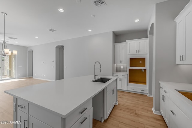 kitchen with white cabinets, sink, hanging light fixtures, an island with sink, and light hardwood / wood-style floors