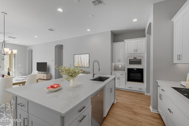 kitchen featuring dishwasher, white cabinets, sink, an island with sink, and black oven