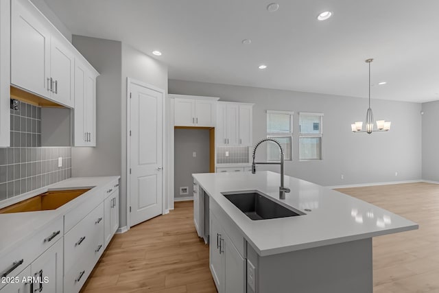 kitchen featuring sink, hanging light fixtures, tasteful backsplash, a center island with sink, and white cabinets