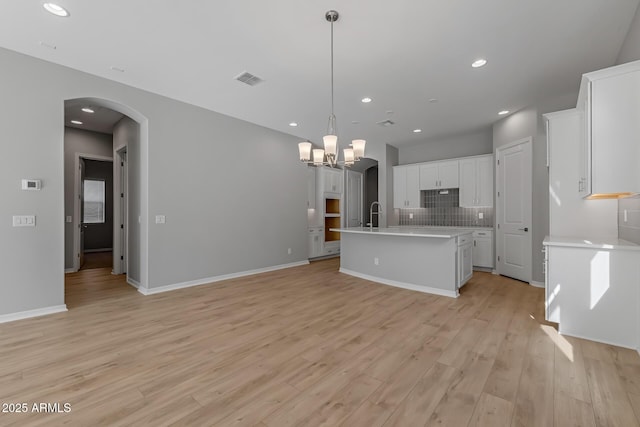 kitchen with a kitchen island with sink, pendant lighting, light hardwood / wood-style floors, decorative backsplash, and white cabinets