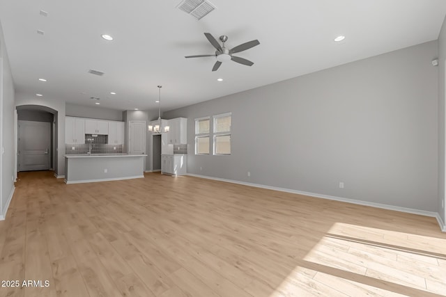 unfurnished living room with ceiling fan with notable chandelier and light hardwood / wood-style floors