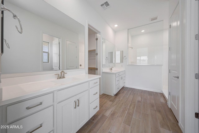 full bath featuring visible vents, wood finished floors, two vanities, and a sink