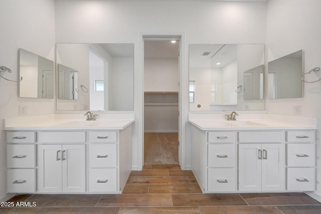 bathroom with a spacious closet, two vanities, wood tiled floor, and a sink