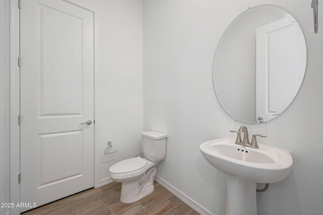 half bathroom featuring toilet, baseboards, and wood finished floors