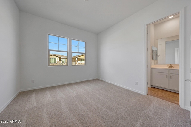 unfurnished bedroom with light colored carpet, ensuite bathroom, baseboards, and a sink