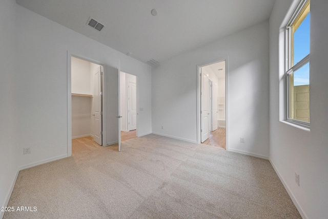 unfurnished bedroom with visible vents, light carpet, baseboards, and a walk in closet