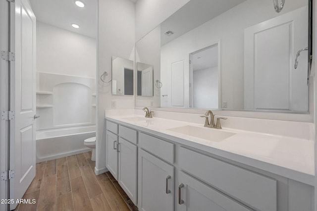 bathroom with double vanity, toilet, wood finish floors, and a sink