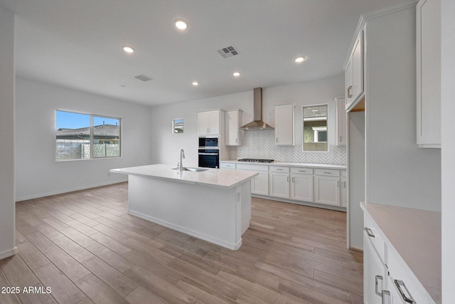 kitchen featuring decorative backsplash, appliances with stainless steel finishes, wall chimney exhaust hood, and light wood finished floors