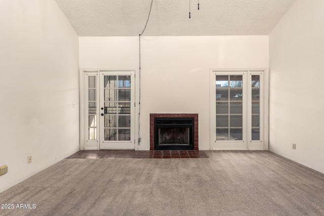 unfurnished living room featuring a tiled fireplace, a healthy amount of sunlight, a textured ceiling, and dark carpet