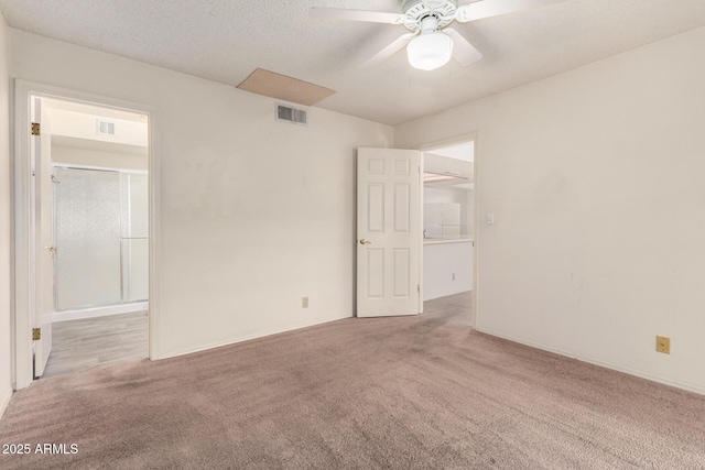 unfurnished bedroom with ceiling fan, a spacious closet, light colored carpet, and a textured ceiling