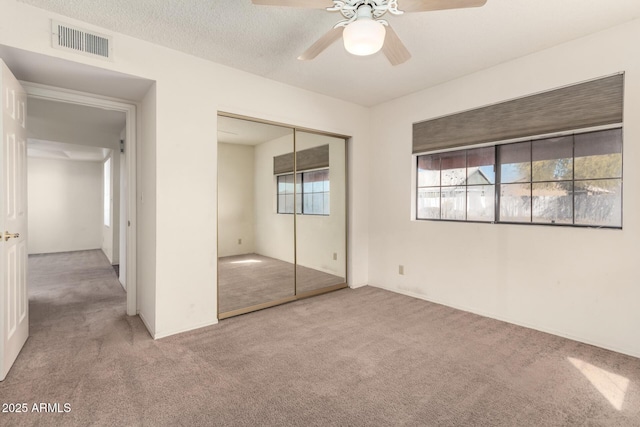 unfurnished bedroom featuring light carpet, ceiling fan, a closet, and a textured ceiling