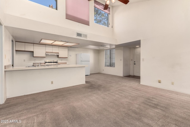 unfurnished living room featuring light carpet, sink, a towering ceiling, and ceiling fan