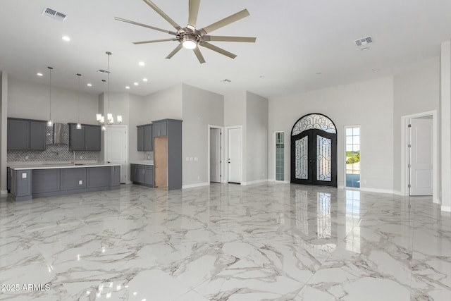 unfurnished living room featuring french doors, visible vents, a high ceiling, and ceiling fan with notable chandelier