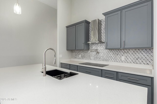 kitchen featuring wall chimney exhaust hood, black electric cooktop, a sink, gray cabinetry, and backsplash