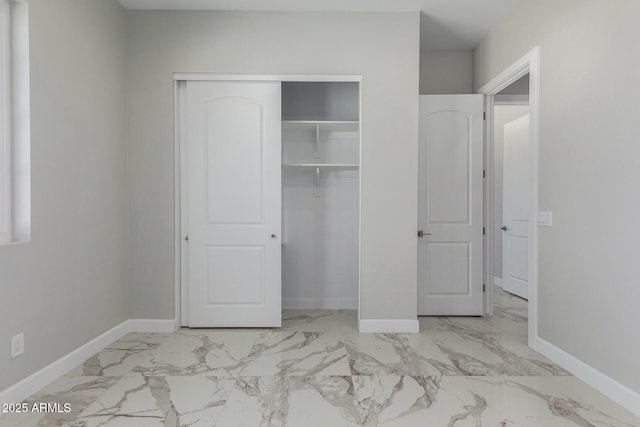 unfurnished bedroom with marble finish floor, a closet, and baseboards