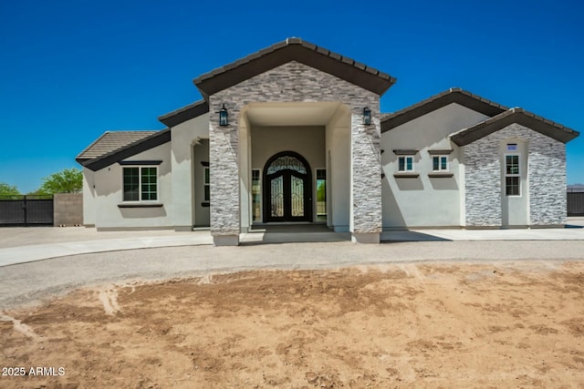 view of front of property featuring stucco siding, french doors, stone siding, a tiled roof, and fence